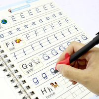 Handwriting practice book with letters E, F, G, and H being written by a hand holding a pen.